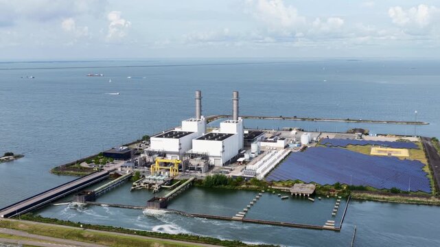 Aerial view of the Maxima power plant featuring industrial buildings, tall chimneys, and a large solar panel array situated on the coast in Lelystad, Flevoland, Netherlands.