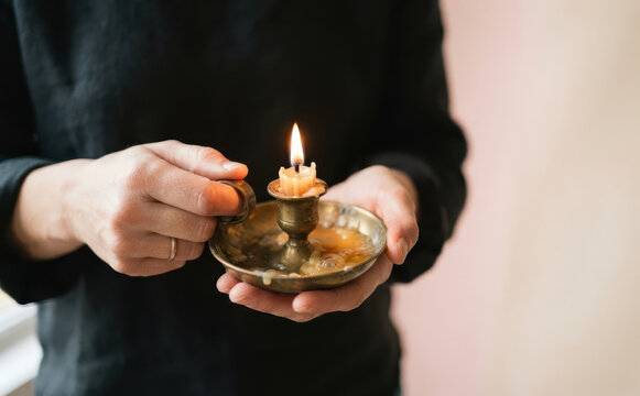 Person holding a burning candle in a vintage brass candlestick holder, representing hope, peace, and spiritual meditation