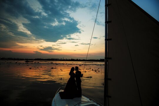 Romantic couple silhouette on sailboat prow at sunset twilight
