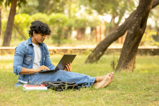Indian college male student studying at park while using laptop