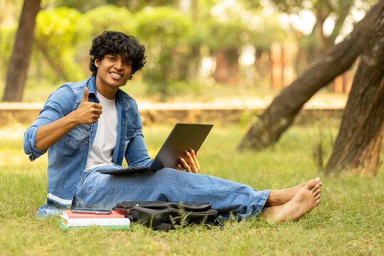 Indian college male student studying at park while using laptop