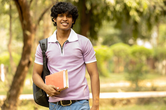 Portrait of indian young college student with backpack and notebooks standing and smiling in park