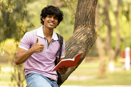 Portrait of indian young college student with backpack and notebooks standing and smiling in park