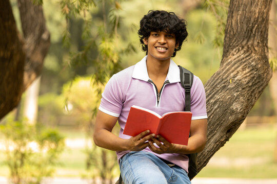 Portrait of indian young college student with backpack and notebooks standing and smiling in park