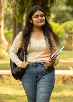 Portrait of indian young girl college student with backpack and notebooks standing and smiling in park