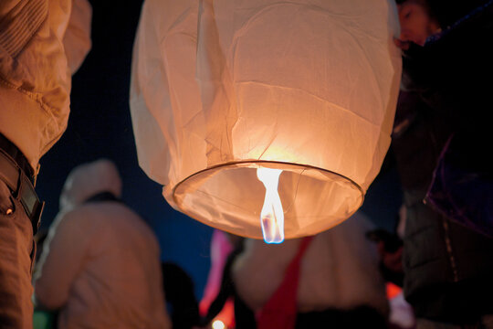 A close-up shot of a person holding a lit sky lantern against the dark night sky, preparing to release it into the air during a traditional festival or celebration.