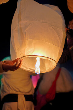 A close-up shot of a person holding a lit sky lantern against the dark night sky, preparing to release it into the air during a traditional festival or celebration.