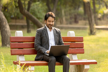 Fototapeta premium Indian Young businessman is sitting at the park and using laptop. Businessman using laptop outdoor