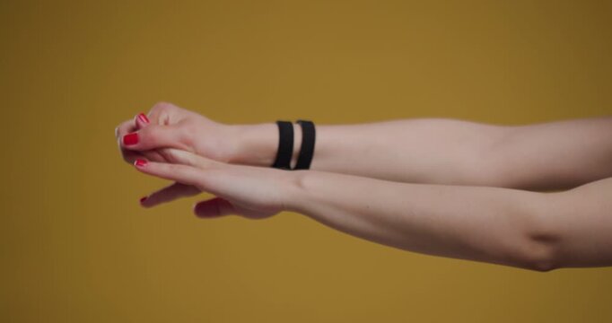 Abstract view of a young woman's hands with red nails, stretching against a yellow background