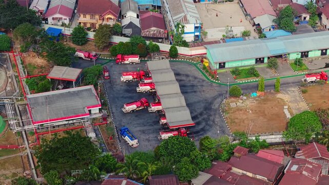 Aerial view of PT. Pertamina TBBM Samarinda fuel depot with red tanker trucks parked under a canopy in Samarinda, East Kalimantan, Indonesia.