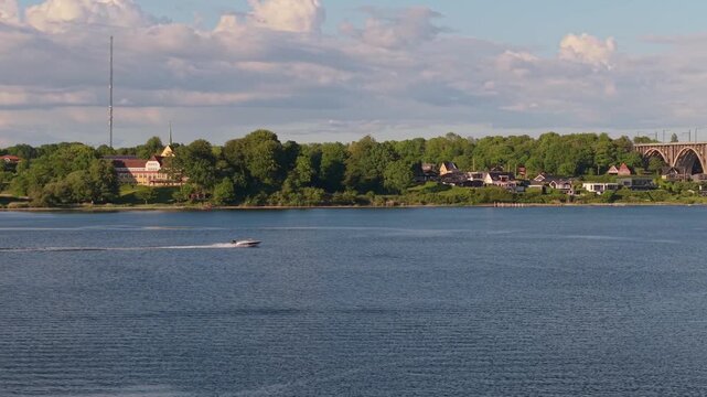 Aerial drone footage following a speedboat along Middelfart's scenic coastline as it heads toward the iconic Old Little Belt Bridge over the Little Belt Strait.
