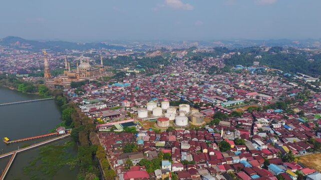 Aerial view of PT. Pertamina TBBM Samarinda fuel storage tanks surrounded by dense urban housing and the Islamic Center Mosque in Samarinda, East Kalimantan, Indonesia.