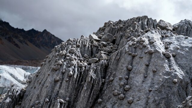 Rugged rock formation with rounded nodules in a mountainous, glacial landscape under overcast skies