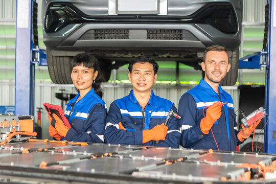 Team of electric vehicle technicians standing with an EV battery pack in an automotive workshop, representing skilled workforce, battery maintenance, engineering, teamwork