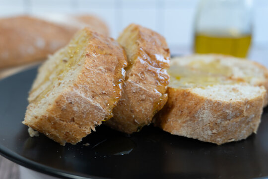 Fresh bread slices glisten with golden oil. Served on a dark plate, they look warm and inviting. Soft crust and tender crumb invite a satisfying bite