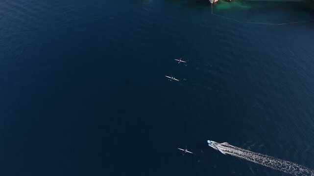 Aerial view of rowers in small boats gliding across the deep blue sea near the rocky coastline of Rijeka, Primorje-Gorski Kotar, Croatia.