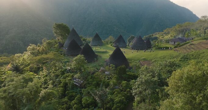 Aerial view of the traditional cone-shaped houses of Waerebo Village nestled in the lush green mountains of Satar Mese Barat, East Nusa Tenggara, Indonesia.
