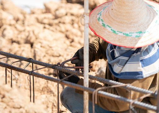 Close-up of an ironworker wearing protective gloves tying steel reinforcement bars for a building's concrete foundation framework.