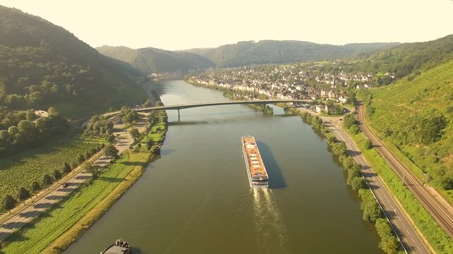Aerial view of a cruise ship sailing on the Moselle River past a town with vineyards, a bridge, and railway tracks in Duisburg, North Rhine-Westphalia, Germany.