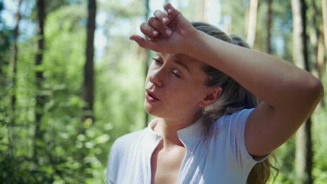 Woman stands in sunlit forest, eyes wide, breathes deeply. She looks upward, enjoying peaceful moment. Forest glows with green, trees tall and dense. Suitable for wellness, nature retreats