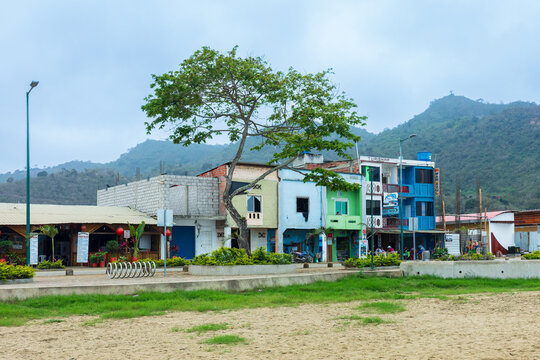 A charming street view with colorful colonial-style buildings, stone-paved promenade, and lush green hills in the coastal town of Puerto L&oacute;pez, Ecuador.
