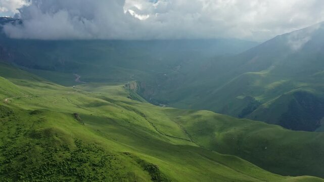 Aerial view of the Caucasus Mountains and Mount Elbrus with lush green slopes, rolling hills, and dramatic clouds in Russia.