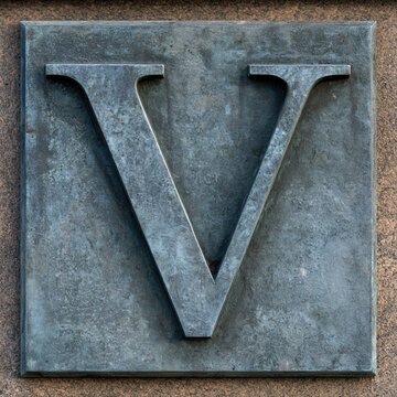 Embossed letter V on weathered metal and stone textured background