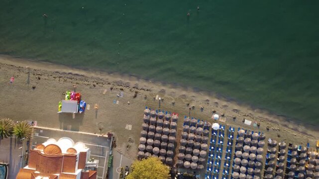 Aerial view of the beach with a wooden pier, rows of sun umbrellas, and calm sea water in Paralia Katarinis, Greece.