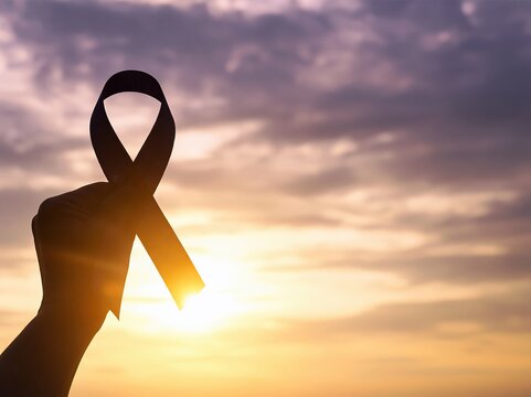 Ribbon held by a hand in silhouette against a golden sunset representing cancer awareness hope