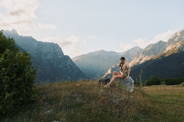 Obraz premium Joyful woman outdoors, seated on a meadow with mountain backdrop, warm sunlight, casual attire, relaxed posture, tranquil nature scene, gentle breeze, vibrant colors, lifestyle moment