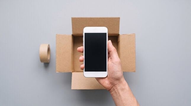 Main tenant un smartphone au-dessus d&rsquo;une bo&icirc;te en carton ouverte vue de dessus