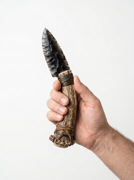 A hand holding a primitive obsidian stone knife with an antler handle.