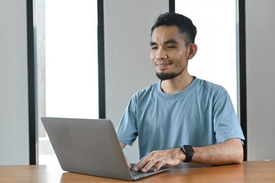 A cheerful man working on a computer from home, enjoying a comfortable workspace and the flexibility of online work.
