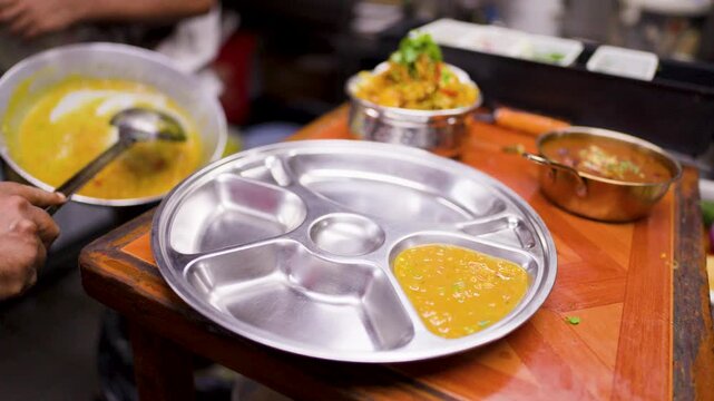 Chef Serving Hot Lentil Dal Curry Onto Stainless Steel Thali Plate