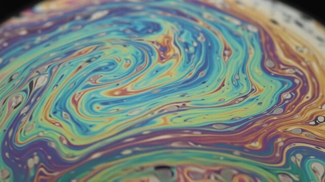 Abstract macro background of iridescent swirling fluid colors on a liquid soap bubble surface showing psychedelic interference patterns