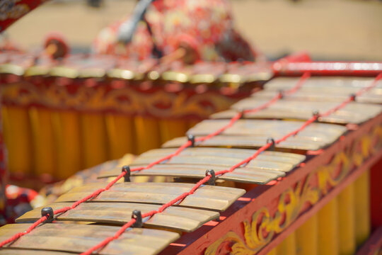 A close-up shot of a traditional Javanese gamelan musical instrument with mallets resting on it, played by musicians wearing batik shirts and blangkon during a cultural festival.