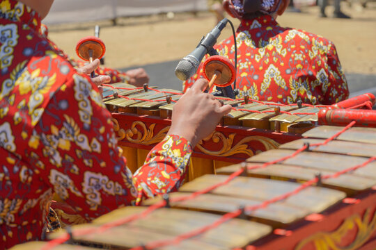 A close-up shot of a traditional Javanese gamelan musical instrument with mallets resting on it, played by musicians wearing batik shirts and blangkon during a cultural festival.