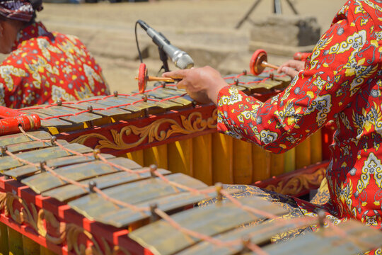 A close-up shot of a traditional Javanese gamelan musical instrument with mallets resting on it, played by musicians wearing batik shirts and blangkon during a cultural festival.