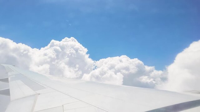4K 60fps POV shot from a passenger airplane window showing the aircraft wing flying close to and momentarily passing through large, bright white cumulus clouds against a blue sky over Istanbul.