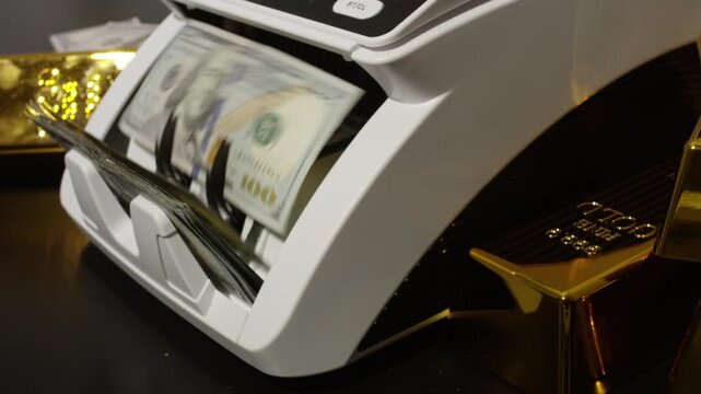 Money counting machine processing hundred dollar bills. Cash count in motion. Gold bars and US dollars. Cash counting action. Banking operation with counting money and gold.