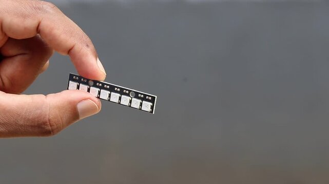 hand holding small pcb strip with row of argb led diodes electronic component close up shot