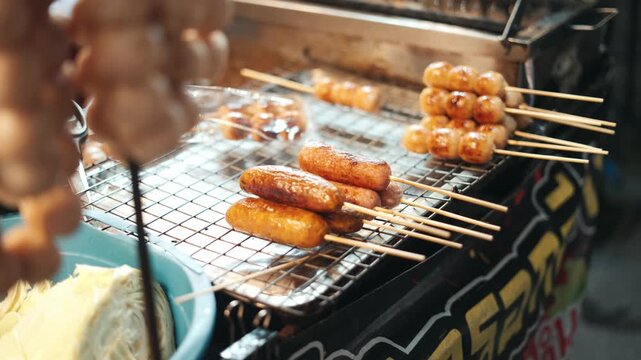 Street vendor cooking traditional sausages and meatball skewers on a grill at a night market