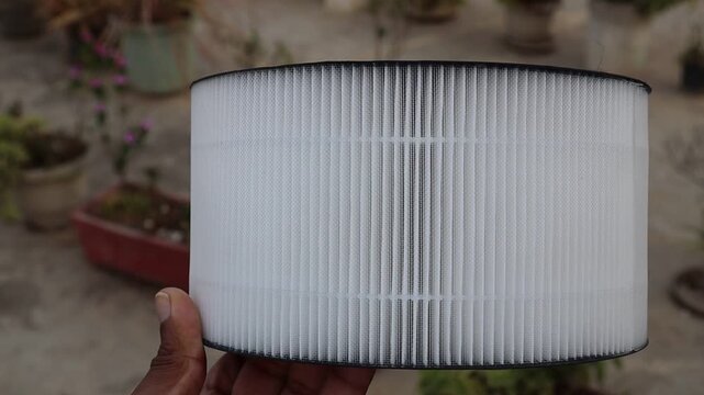 Hand holding indoor air purifier filter cartridge showing pleated details close up view
