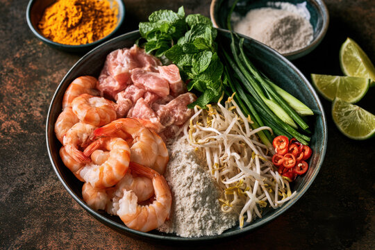 Asian cooking ingredients with prawn, pork, sprout, mint, onion, chilli, lime, turmeric and flour arranged in a ceramic bowl for a vibrant savoury recipe.