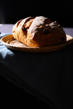 Sourdough bread loaf with dried fruit on a woven plate with light and shadow, healthy homemade food