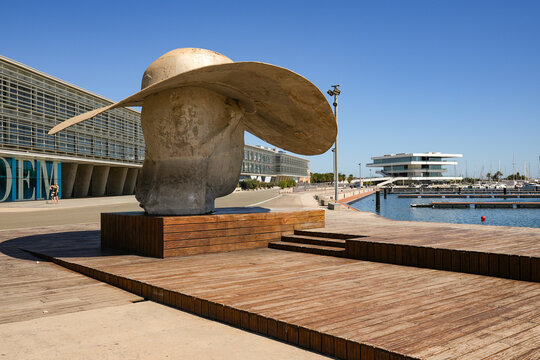 The monumental sculpture "La Pamela" by artist Manolo Vald&eacute;s at the Marina de Valencia waterfront. Giant head with a sun hat with modern architecture Veles e Vents in the background.
