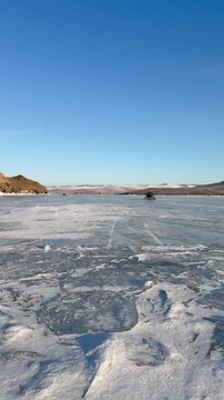 Vertical video of frozen Baikal Lake on February sunny day. Tourists travel on ice of Small Sea in an airboat to Olkhon Island. Ice trips and adventure