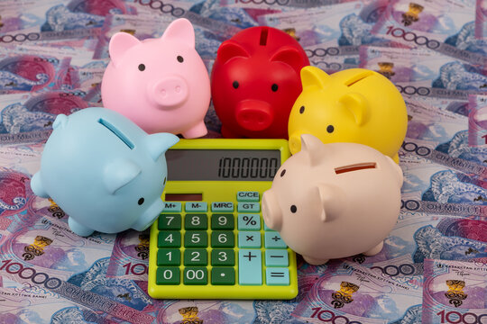 Piggy banks and a calculator against a background of 10000 Kazakhstani tenge banknotes.