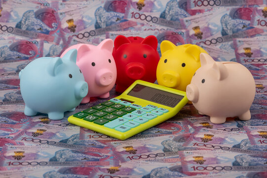 Piggy banks and a calculator against a background of 10000 Kazakhstani tenge banknotes.