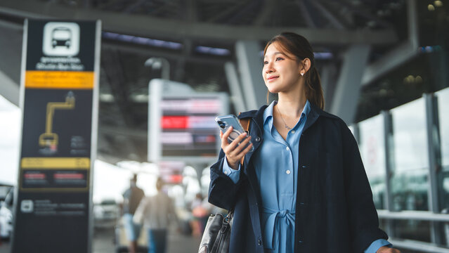 Young adult asian woman with travel luggage using smartphone app call taxi service transfer at international airport shuttle bus terminal
